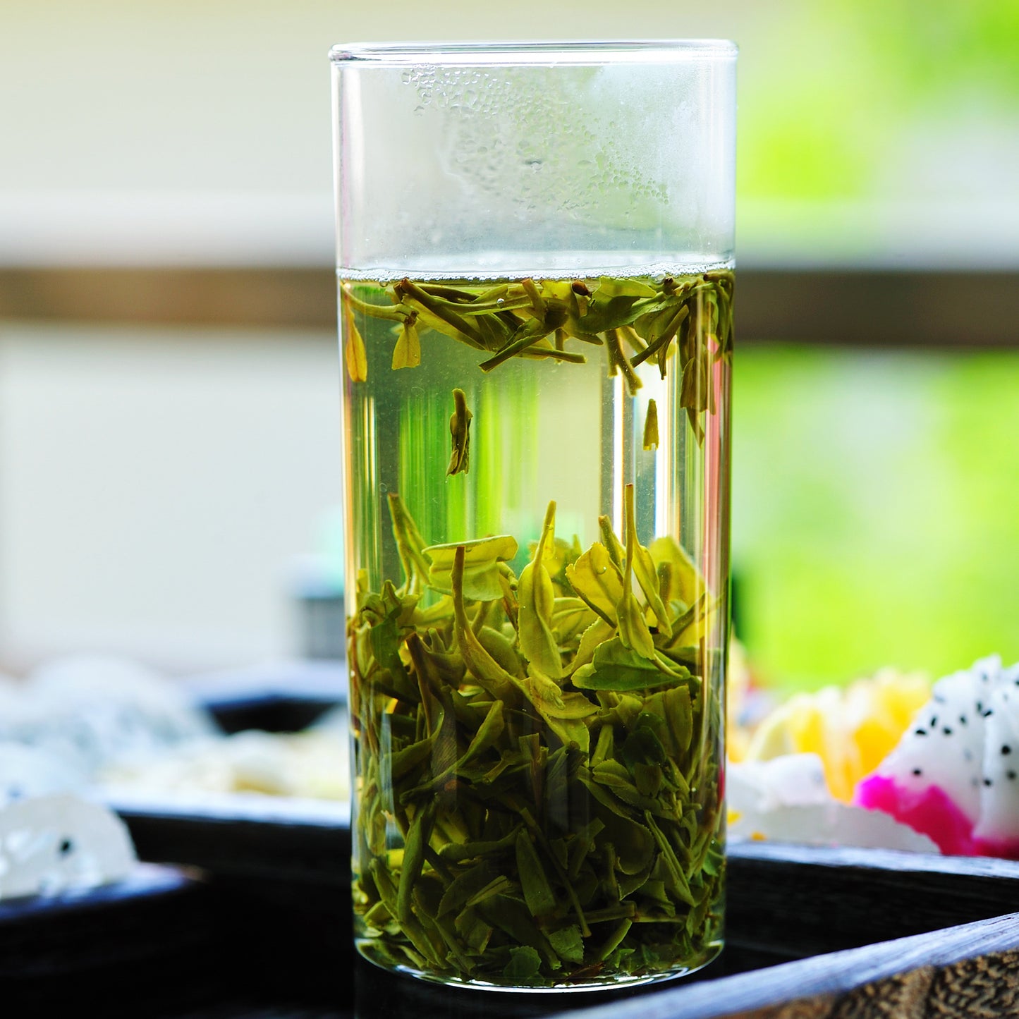 Clear glass container with dragonwell tea leaves on a blurred natural background