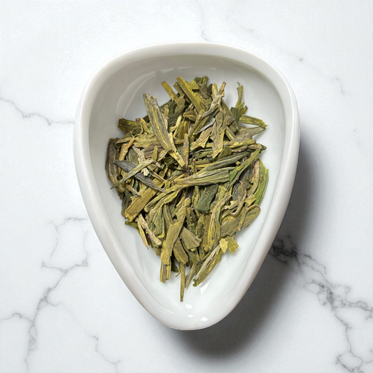 Dragonwell tea leaves in a white ceramic dish on a marble surface