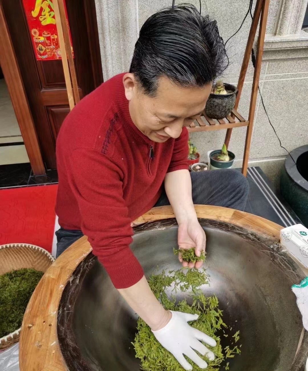 Person in a red shirt and white gloves pan-firing dragonwell tea leaves in a wok