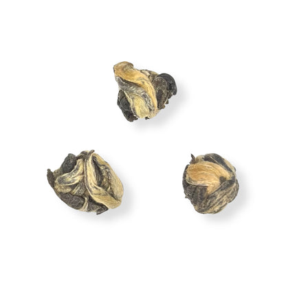 Three hand-rolled jasmine green tea pearls, in a natural state, isolated on a white background.