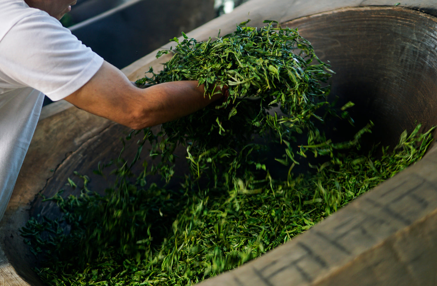 a tea master heating and tossing tea leaves in a giant wok